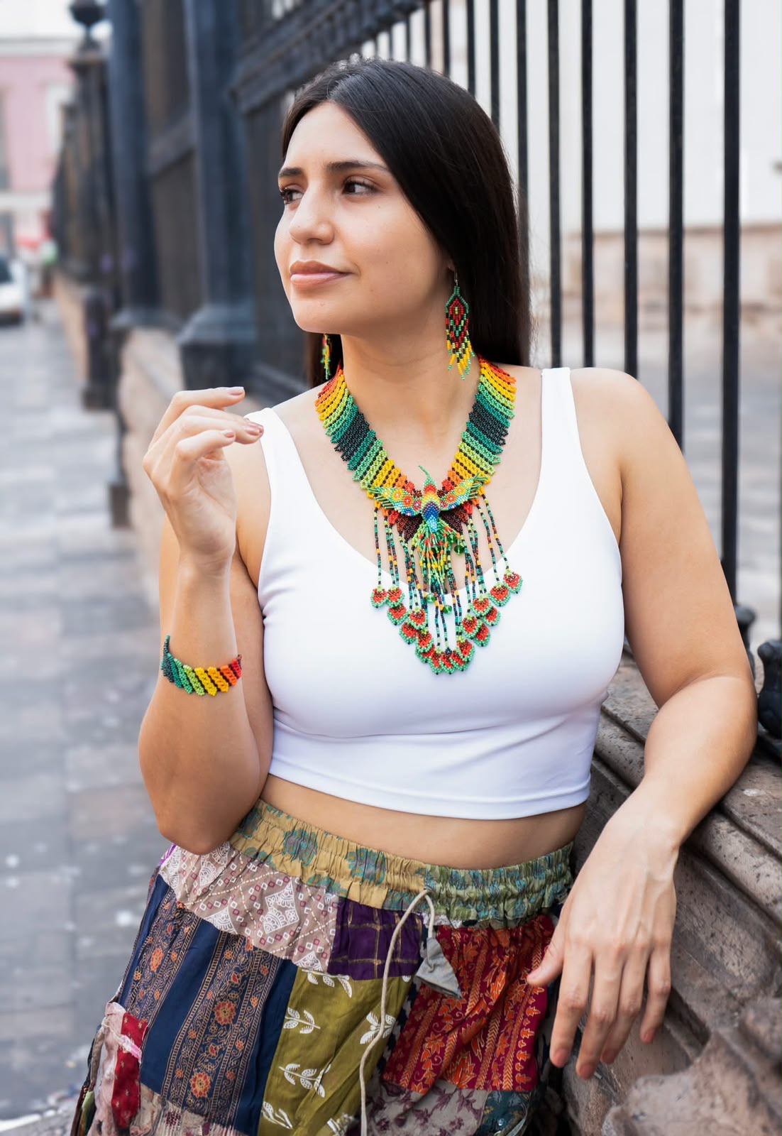 Collar, pendientes y pulsera de cuentas multicolores con una blusa blanca.